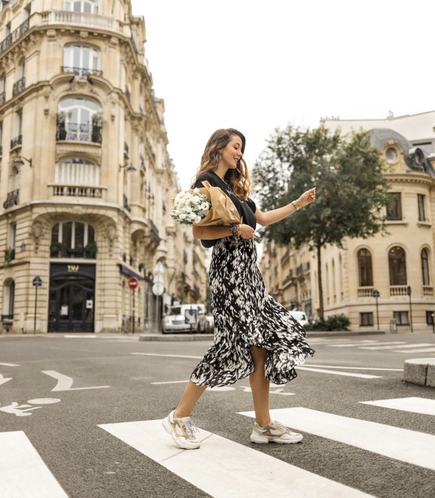 Look féminin pour porter des tennis longue jupe imprimée asymétrique, T-shirt noir et bouquet de fleurs dans les rues parisiennes 