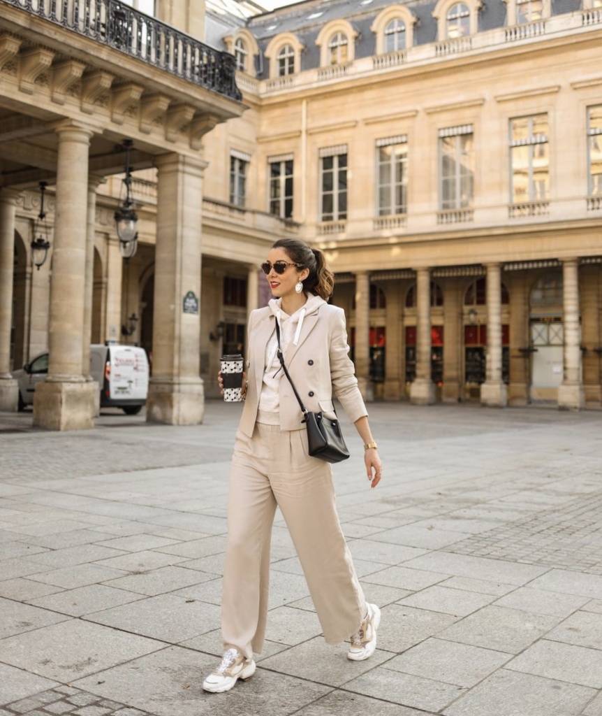 Look working girl pour porter des baskets et aller travailler tailleur ensemble blazer et pantalon beige sweat à capuche blanc et lunettes de soleil